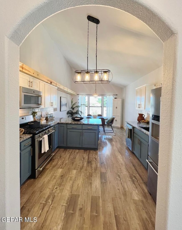 kitchen with appliances with stainless steel finishes, kitchen peninsula, light hardwood / wood-style floors, lofted ceiling, and decorative light fixtures