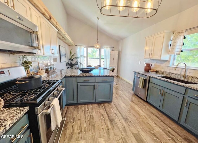 kitchen featuring lofted ceiling, light hardwood / wood-style flooring, stainless steel appliances, sink, and decorative light fixtures