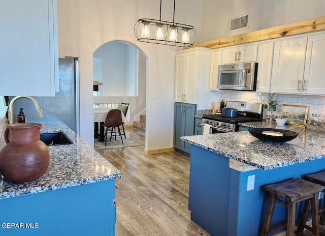 kitchen with white cabinets, hanging light fixtures, appliances with stainless steel finishes, light hardwood / wood-style flooring, and sink