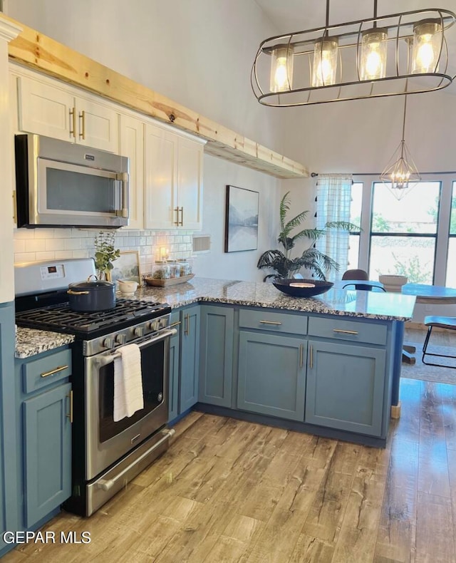 kitchen featuring appliances with stainless steel finishes, blue cabinets, hanging light fixtures, and light wood-type flooring