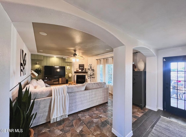 living room with ceiling fan, a textured ceiling, and a large fireplace