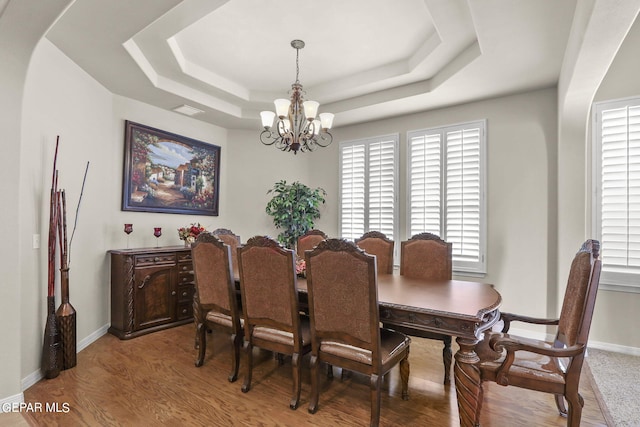 dining area with hardwood / wood-style flooring, a raised ceiling, and a chandelier