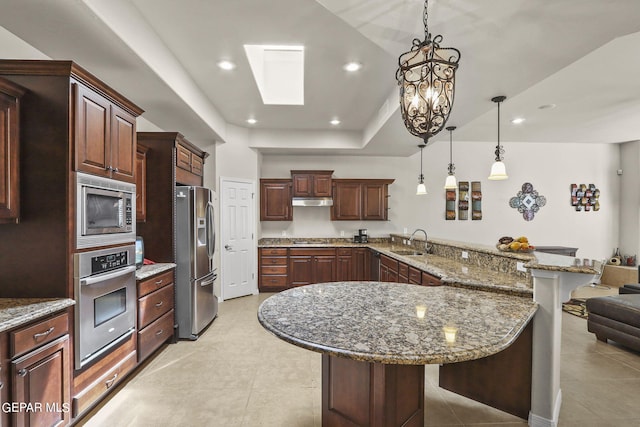 kitchen with appliances with stainless steel finishes, a breakfast bar, sink, pendant lighting, and dark stone countertops