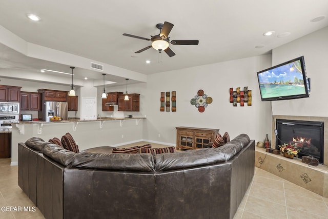 living room featuring ceiling fan, a fireplace, and light tile patterned flooring