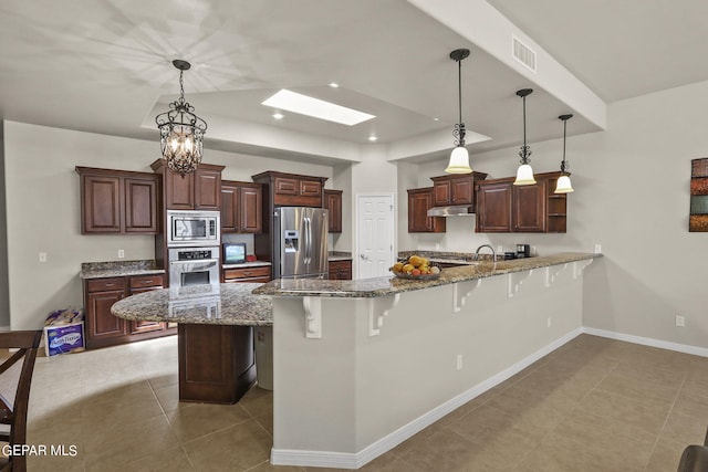 kitchen with appliances with stainless steel finishes, a skylight, dark stone counters, decorative light fixtures, and a breakfast bar area