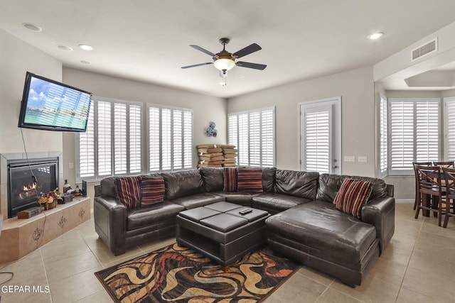 living room with ceiling fan, a tile fireplace, light tile patterned floors, and a wealth of natural light