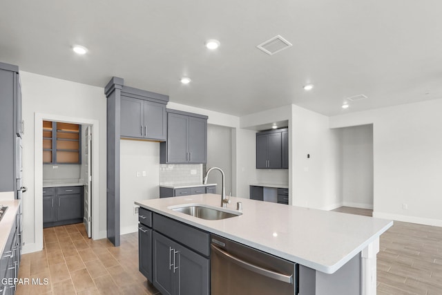 kitchen with gray cabinetry, sink, an island with sink, light hardwood / wood-style floors, and dishwasher