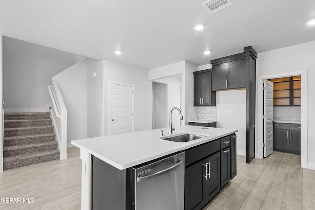 kitchen featuring dishwasher, sink, tasteful backsplash, an island with sink, and light wood-type flooring