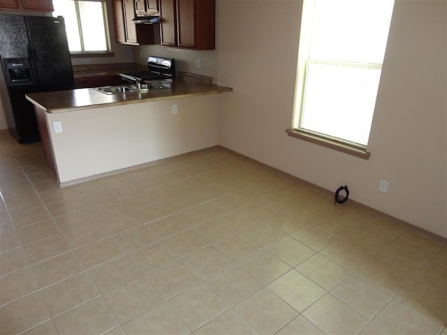 kitchen with black fridge, kitchen peninsula, stove, sink, and light tile patterned flooring