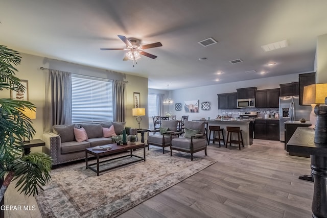 living room featuring light wood-type flooring and ceiling fan with notable chandelier