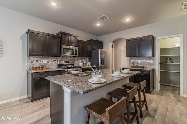 kitchen featuring a center island with sink, stainless steel appliances, backsplash, sink, and a kitchen breakfast bar