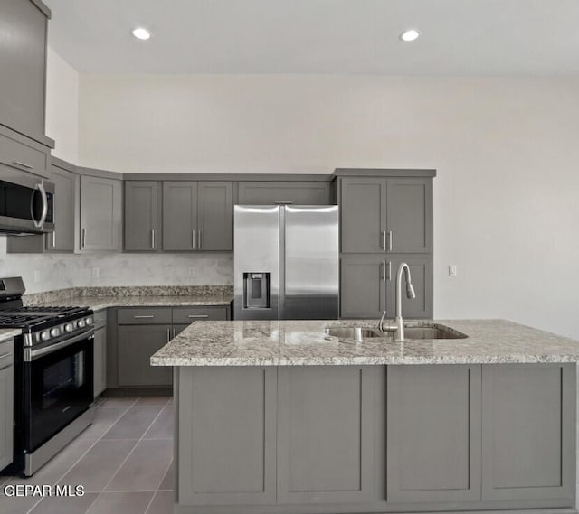 kitchen featuring a kitchen island with sink, gray cabinets, stainless steel appliances, and light stone counters