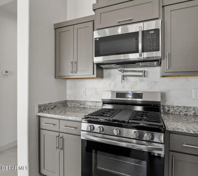 kitchen with light stone countertops, gray cabinetry, backsplash, and appliances with stainless steel finishes