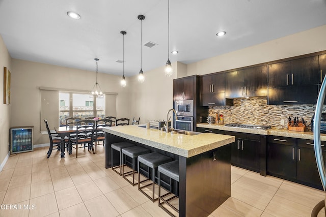 kitchen with stainless steel appliances, sink, an island with sink, a breakfast bar, and decorative light fixtures