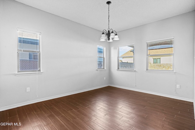 unfurnished room featuring a textured ceiling, dark hardwood / wood-style floors, and a chandelier