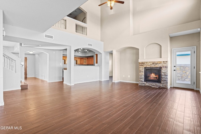 unfurnished living room with a stone fireplace, ceiling fan, wood-type flooring, and a high ceiling