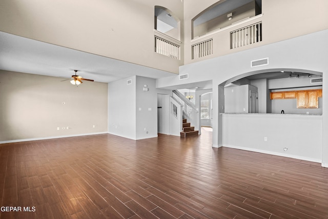 unfurnished living room featuring dark wood-type flooring, ceiling fan, and a towering ceiling