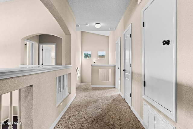 corridor with a textured ceiling, carpet flooring, and vaulted ceiling