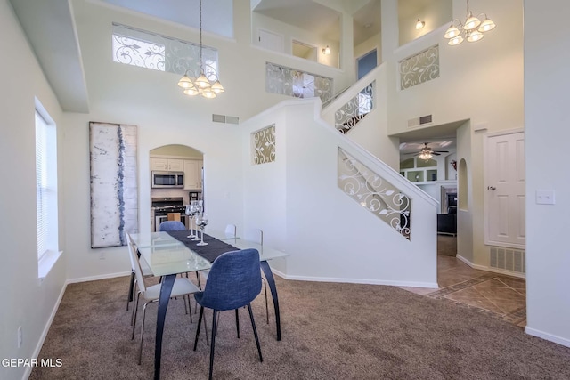 carpeted dining space featuring ceiling fan with notable chandelier and a high ceiling