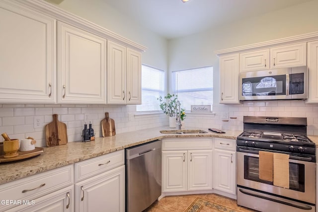 kitchen featuring white cabinets, light tile patterned floors, appliances with stainless steel finishes, tasteful backsplash, and light stone counters