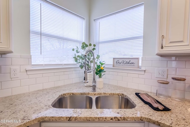 kitchen featuring decorative backsplash, light stone countertops, and sink