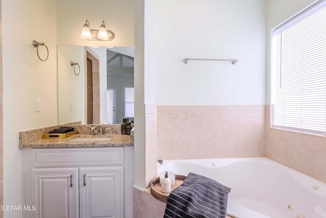 bathroom with tiled tub, vanity, and a healthy amount of sunlight