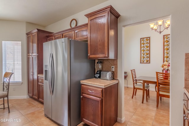 kitchen with tasteful backsplash, light tile patterned floors, pendant lighting, stainless steel refrigerator with ice dispenser, and an inviting chandelier