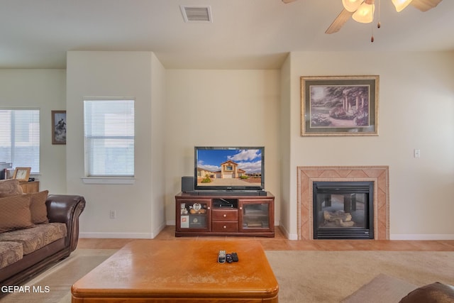 living room with ceiling fan, a tiled fireplace, and light colored carpet