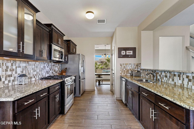 kitchen featuring light stone countertops, light hardwood / wood-style floors, tasteful backsplash, sink, and stainless steel appliances