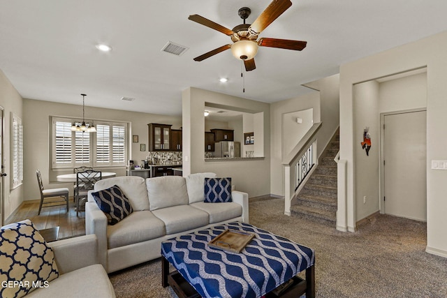 carpeted living room featuring ceiling fan with notable chandelier