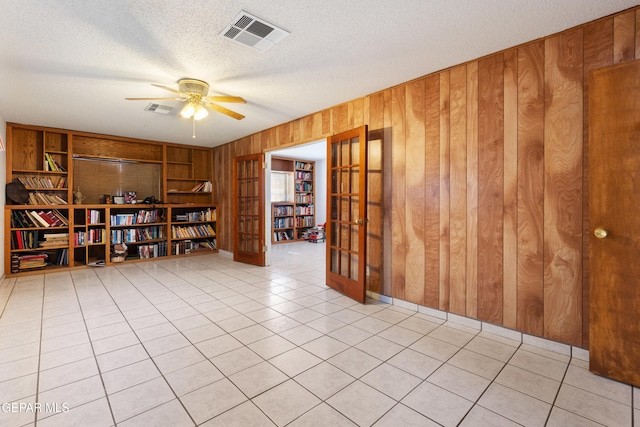 spare room with wood walls, ceiling fan, a textured ceiling, and light tile patterned floors