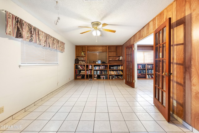 tiled empty room with built in shelves, wooden walls, a textured ceiling, and ceiling fan