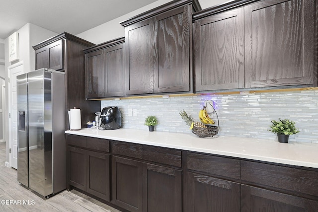 kitchen with dark brown cabinetry, stainless steel refrigerator with ice dispenser, light hardwood / wood-style floors, and decorative backsplash