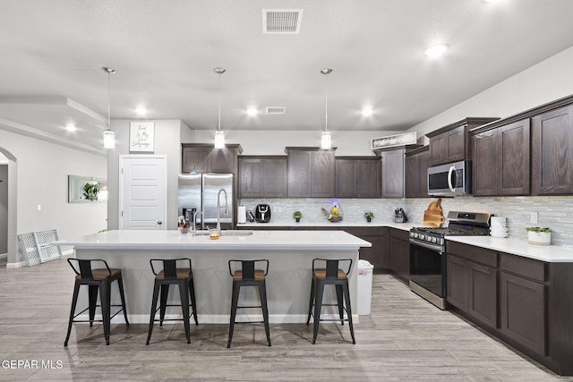 kitchen featuring a kitchen island with sink, a kitchen breakfast bar, stainless steel appliances, and hanging light fixtures