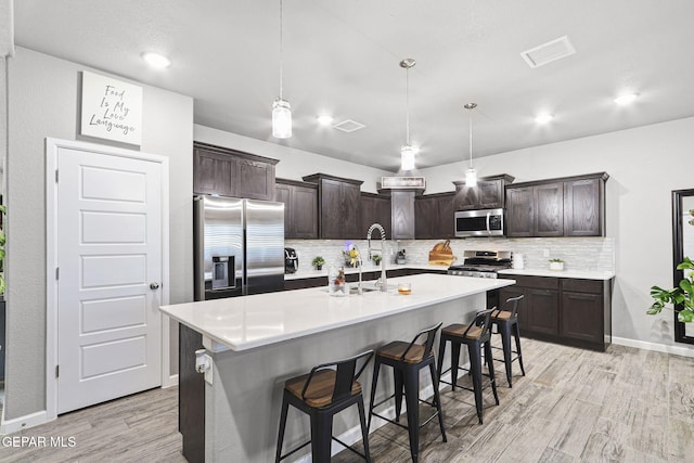 kitchen with pendant lighting, appliances with stainless steel finishes, a center island with sink, and dark brown cabinetry