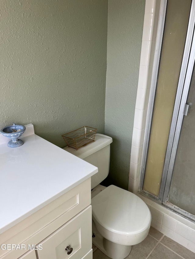 bathroom featuring tile patterned flooring, vanity, toilet, and a shower with shower door