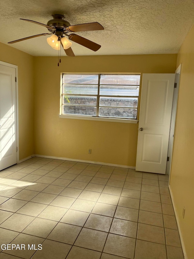 tiled empty room with ceiling fan and a textured ceiling