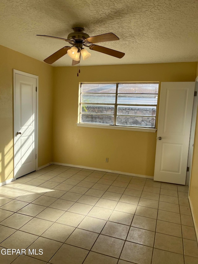 unfurnished room with a textured ceiling, light tile patterned floors, and ceiling fan