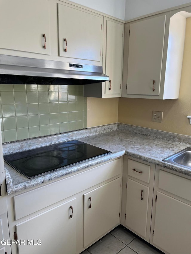 kitchen with white cabinets, light tile patterned floors, black electric cooktop, and sink