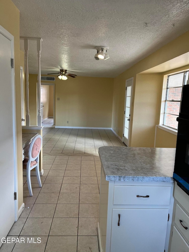 kitchen with light tile patterned flooring, white cabinetry, wall oven, and a textured ceiling