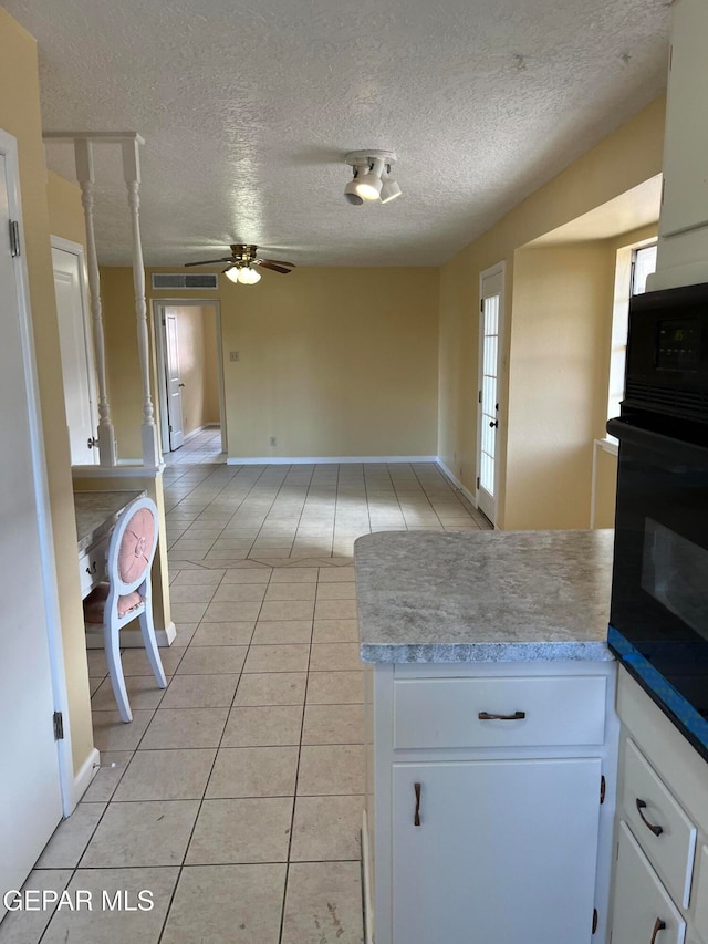 kitchen with light tile patterned flooring, a textured ceiling, white cabinets, oven, and ceiling fan