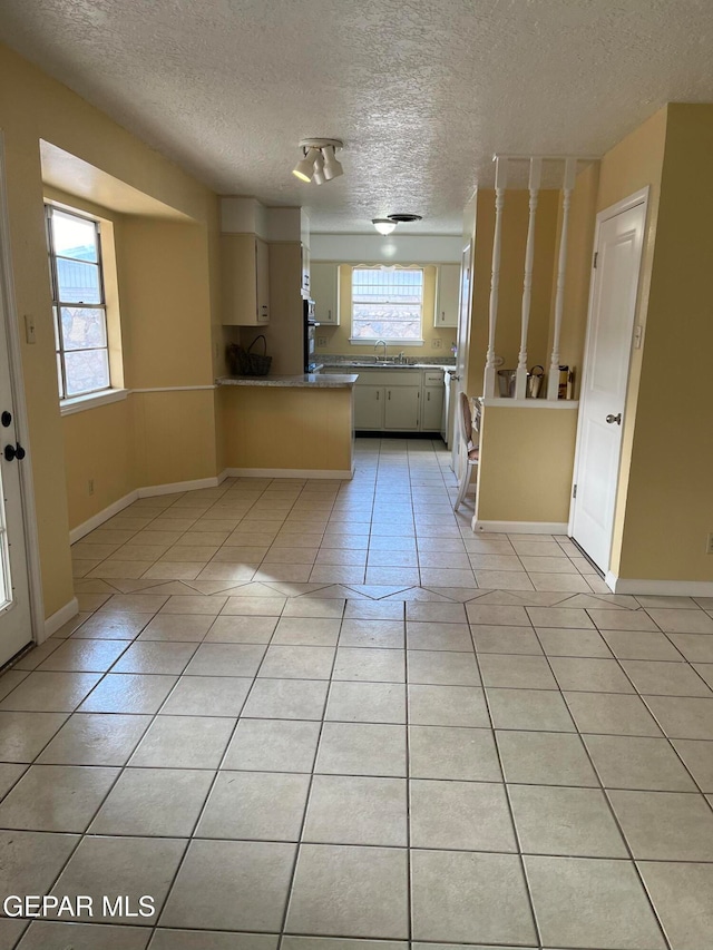 kitchen featuring light tile patterned flooring, a textured ceiling, sink, and kitchen peninsula