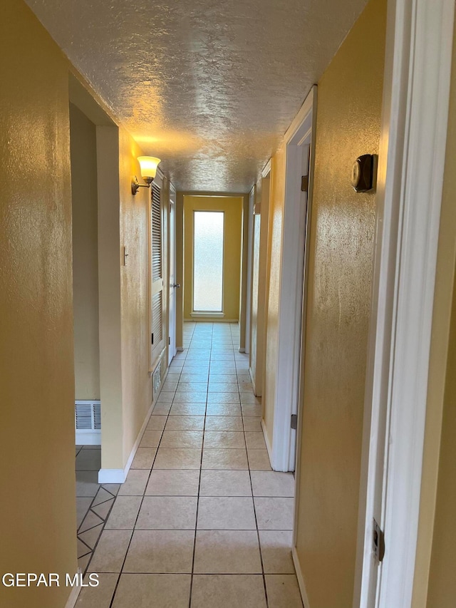 hall with a textured ceiling and light tile patterned floors