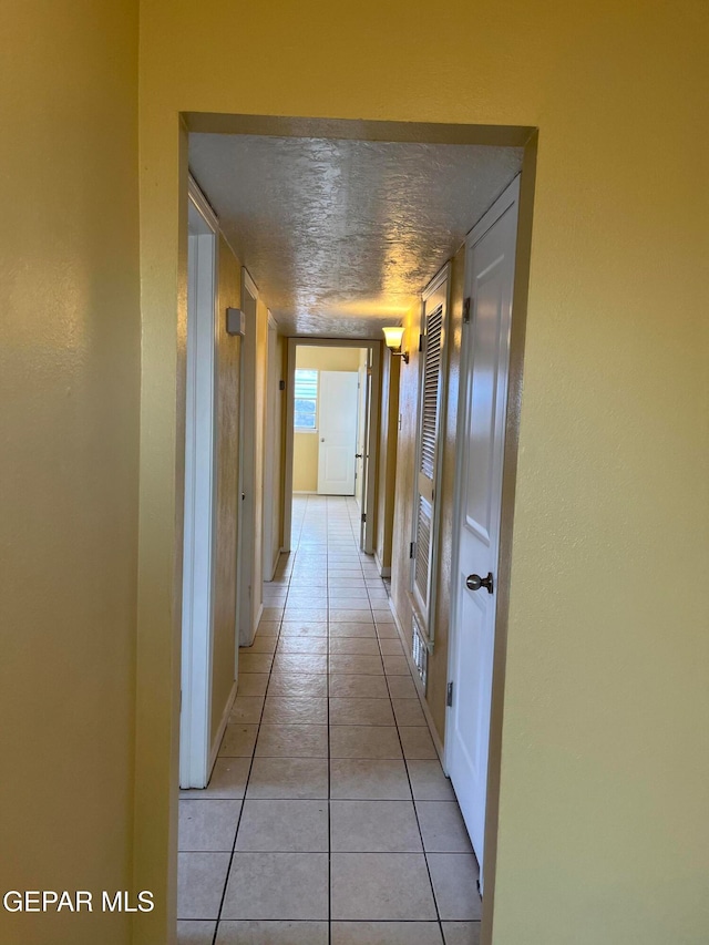 hall with a textured ceiling and light tile patterned floors