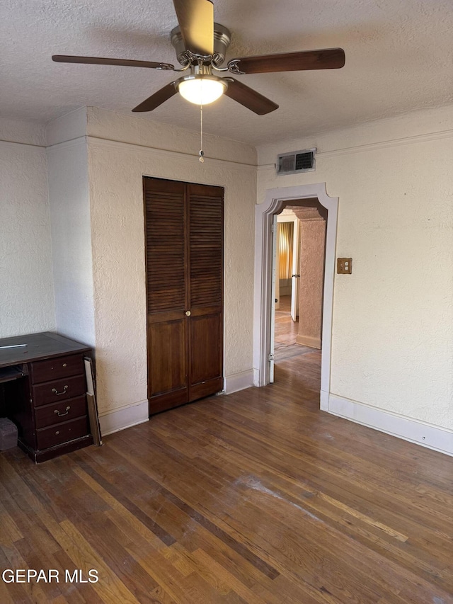 unfurnished bedroom featuring dark hardwood / wood-style floors, ceiling fan, a textured ceiling, and a closet