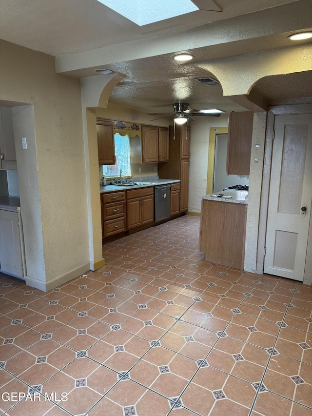 kitchen featuring dishwasher, sink, a skylight, ceiling fan, and light tile patterned floors