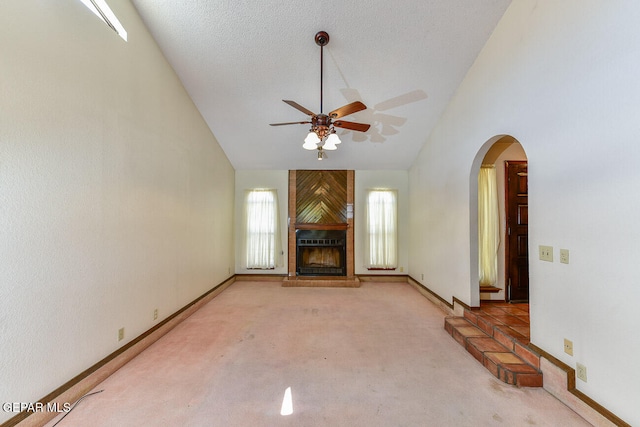 unfurnished living room with carpet floors, a fireplace, a textured ceiling, high vaulted ceiling, and ceiling fan