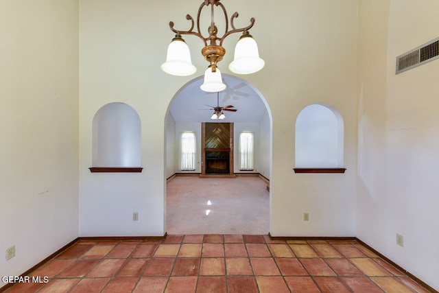 foyer entrance with a fireplace, a high ceiling, and ceiling fan with notable chandelier