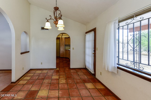 unfurnished dining area featuring high vaulted ceiling, a textured ceiling, an inviting chandelier, and dark tile patterned flooring