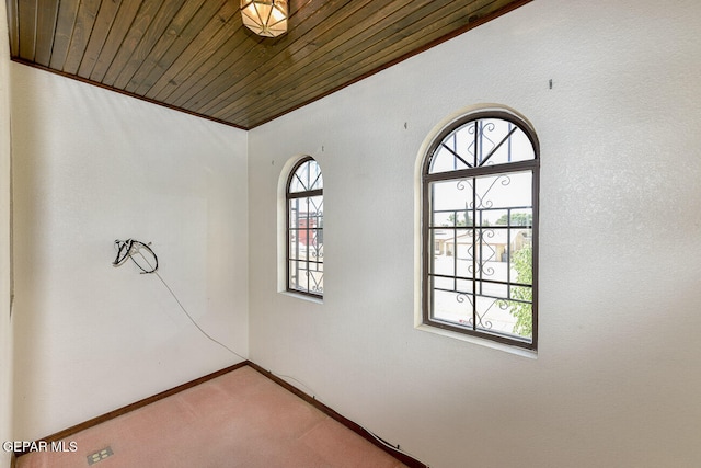 empty room with carpet flooring, a wealth of natural light, crown molding, and wood ceiling